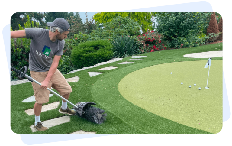 Worker cleaning a synthetic putting green with a turf brush.