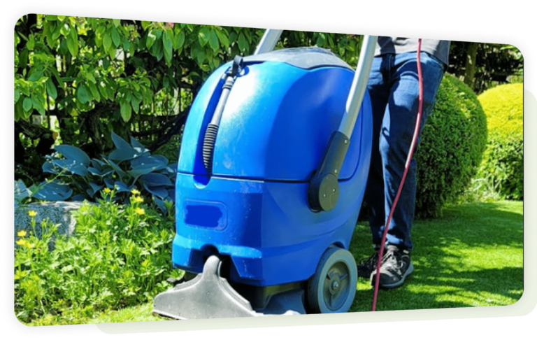 Turf cleaning machine on artificial grass near a landscaped garden.
